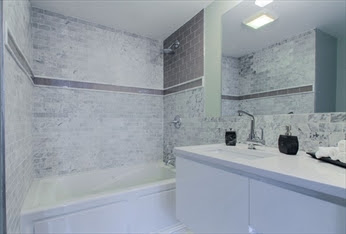 A bathroom with marble walls and floors, and white cabinets.