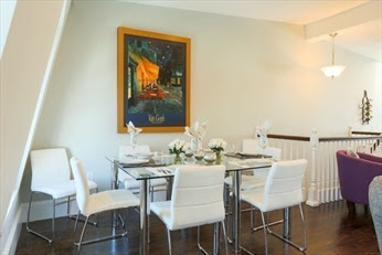 A dining room table with white chairs and a painting on the wall.